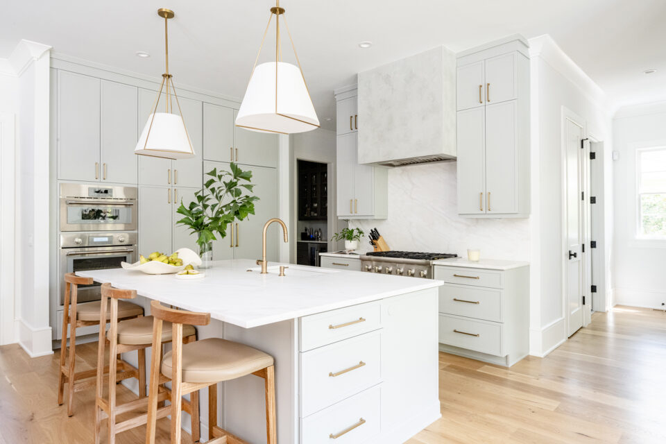 Bright white kitchen with marble island, brass hardware, and large pendant lights over an island.