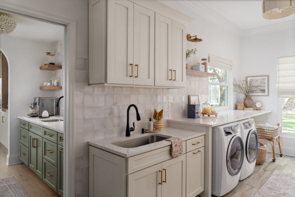 Bright kitchen with white upper cabinets and a stacked washer/dryer in a light-filled laundry nook by a window.