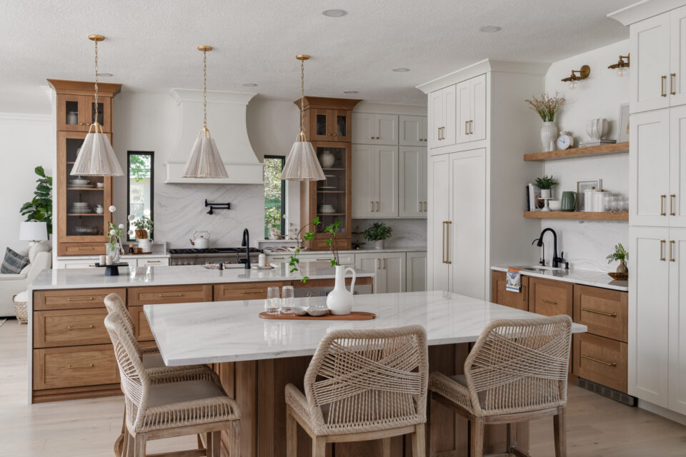 Bright kitchen with white cabinets, marble island, and wooden accents plus woven chairs around the island.