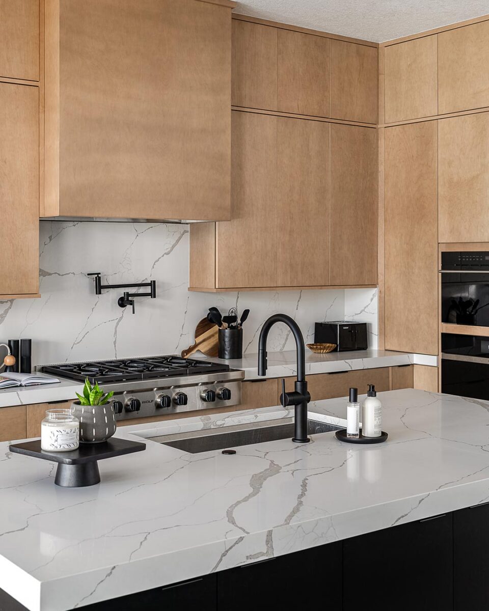 Modern kitchen with light wood cabinets, white marble countertops, and a matte black island faucet centerpiece.