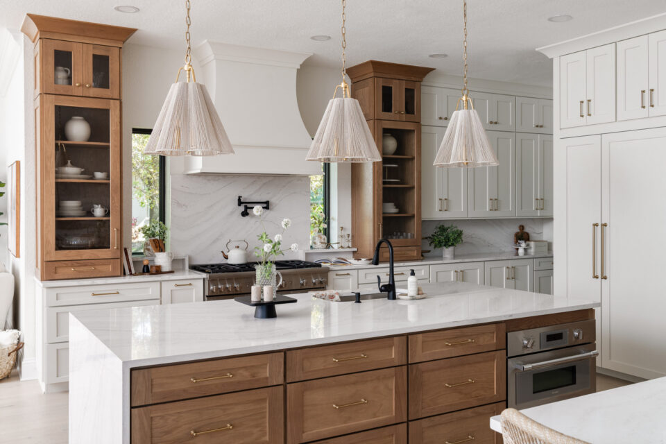 Bright kitchen with white cabinets, marble countertops, a large island, and three woven pendant lights above it.