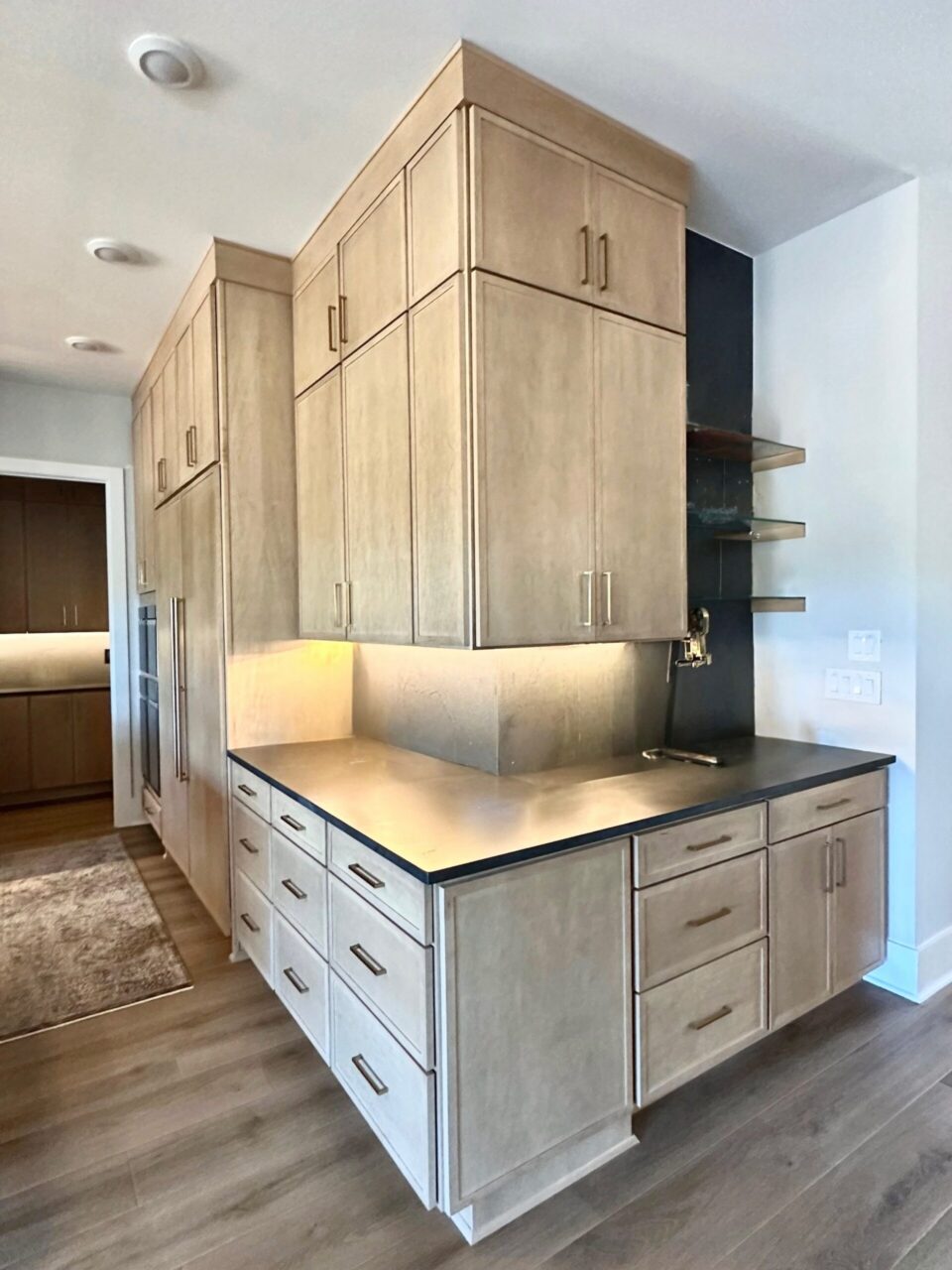 Tall light-wood kitchen cabinets with brushed-metal handles surround a stainless steel island in a modern kitchen.